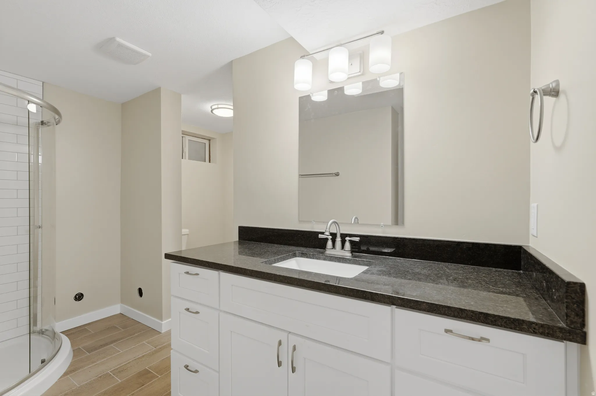 Bathroom featuring a white vanity with brushed nickel hardware, dark stone countertop, undermount sink, and a framed mirror with a four-light fixture