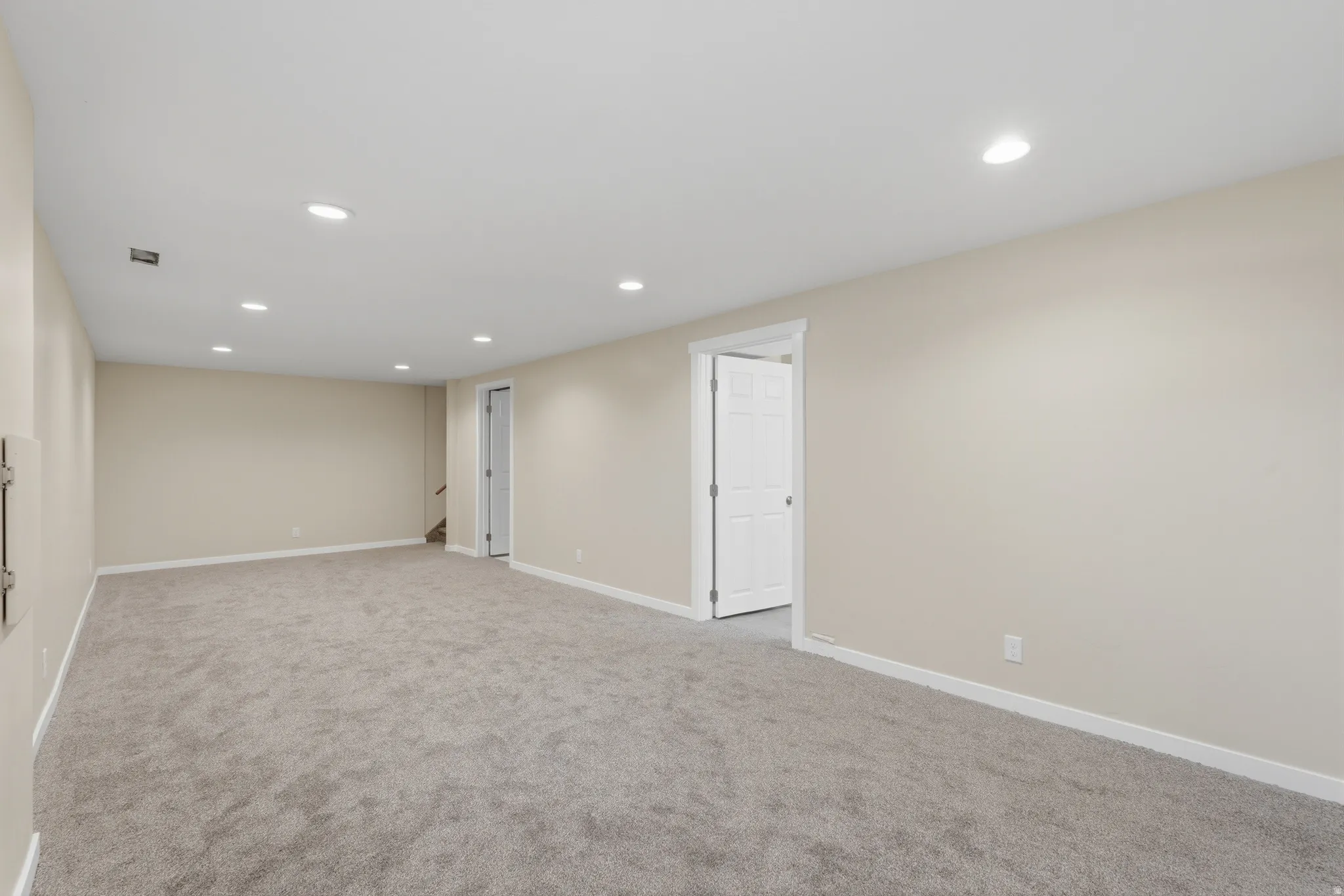 Spacious room featuring neutral carpeting, light-toned walls, recessed lighting, and white trim
