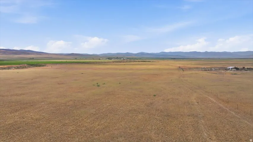 Expansive open land featuring diverse terrain, distant mountains, and agricultural structures