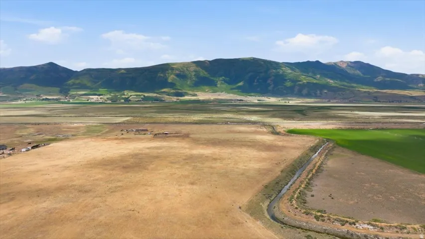 Expansive land parcel featuring a visible irrigation canal and a backdrop of verdant mountains