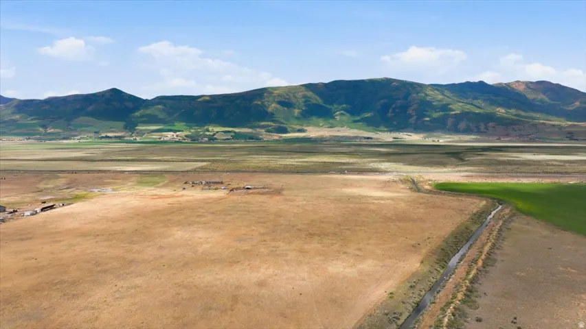 Expansive land parcel featuring a natural water channel, varied terrain, distant mountains, and open skies