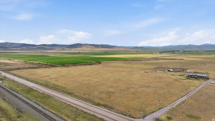 Expansive rural landscape featuring a single-story dwelling, outbuildings, and a gravel road