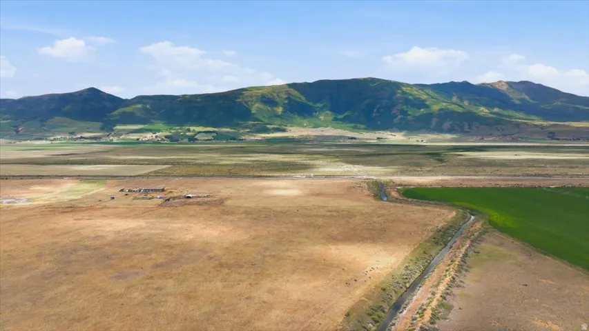 Expansive land parcel featuring a natural water channel, agricultural fields, distant mountain backdrop, and scattered structures