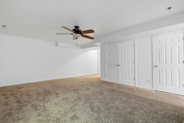 Spacious interior room featuring neutral wall paint, ceiling fan, and carpeted flooring