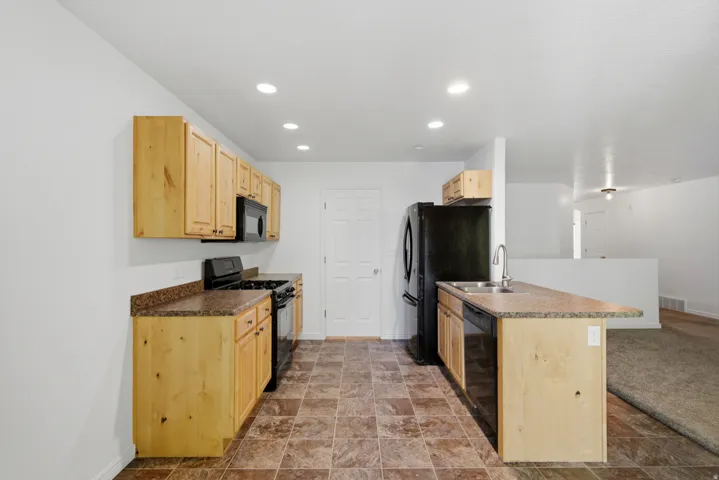 Kitchen featuring light wood cabinetry, stone-finish countertops, and black appliances