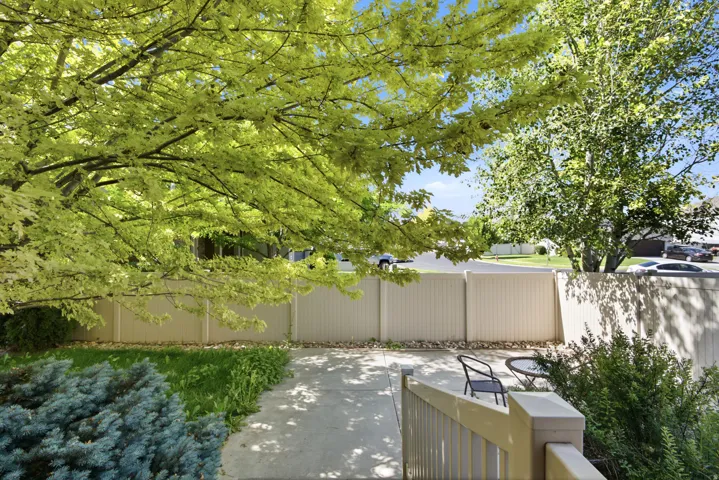Paved patio area featuring a light-toned privacy fence and mature trees