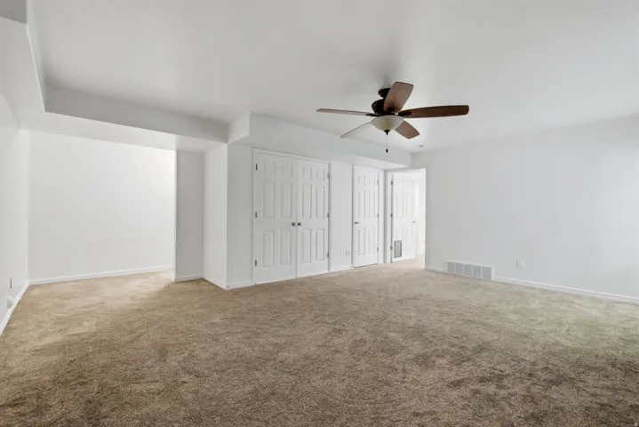 Spacious room with plush brown carpeting, bright white walls, and a ceiling fan with integrated lighting