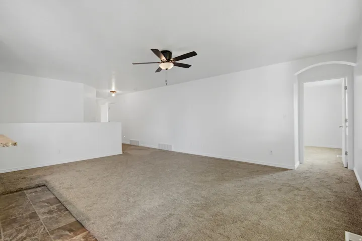 Spacious interior room featuring light beige carpeting, a contemporary ceiling fan, and an arched doorway