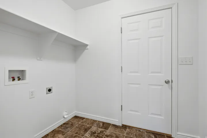 Utility room featuring durable tile flooring, a built-in wall shelf, and paneled interior door