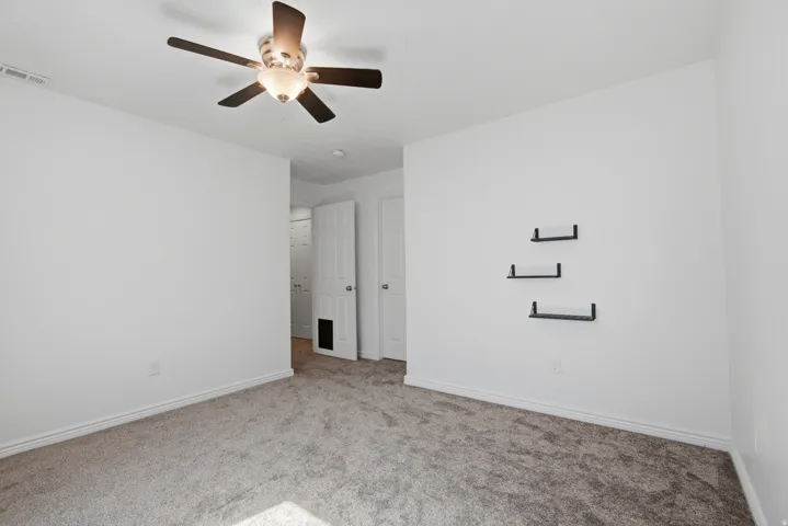 Neutral wall colors with white trim, soft gray carpet, and a ceiling fan with integrated lighting