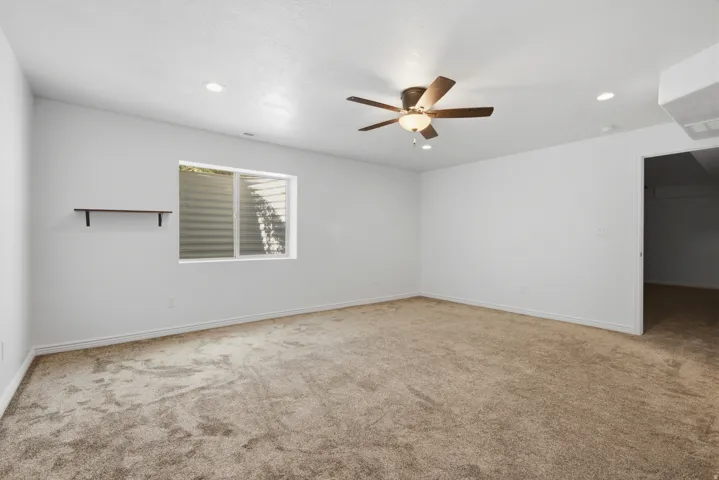 Spacious room featuring neutral carpeting, a ceiling fan with integrated lighting, recessed lighting, a built-in wall shelf, and a window with a window well