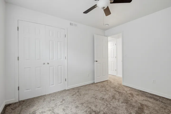 Neutral tone interior featuring a ceiling fan with integrated lighting, white walls, and gray carpet flooring