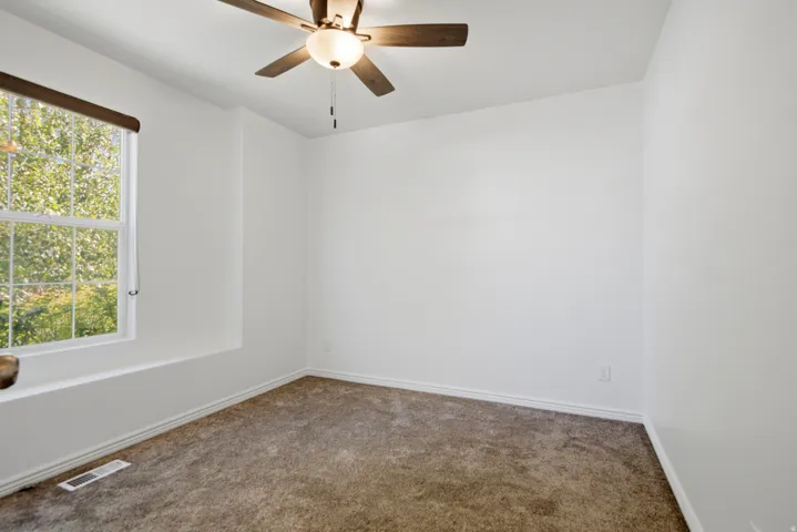 Bright room featuring a large window, neutral carpeting, white baseboards, and a ceiling fan with integrated lighting