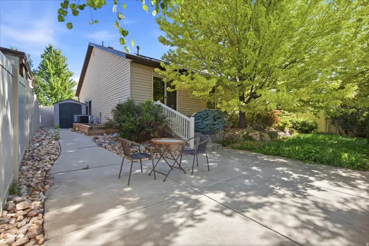 Concrete patio and walkway with gravel accents, framed by a light-colored privacy fence and mature landscaping