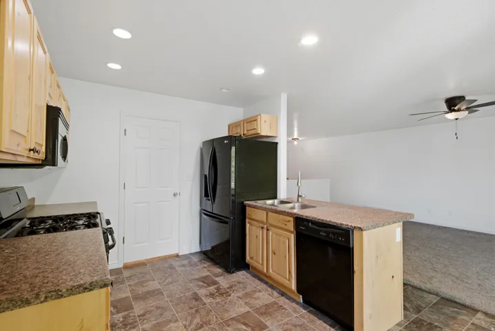 Kitchen featuring wood cabinetry, black appliances including a refrigerator, range, and dishwasher, and a double basin stainless steel sink