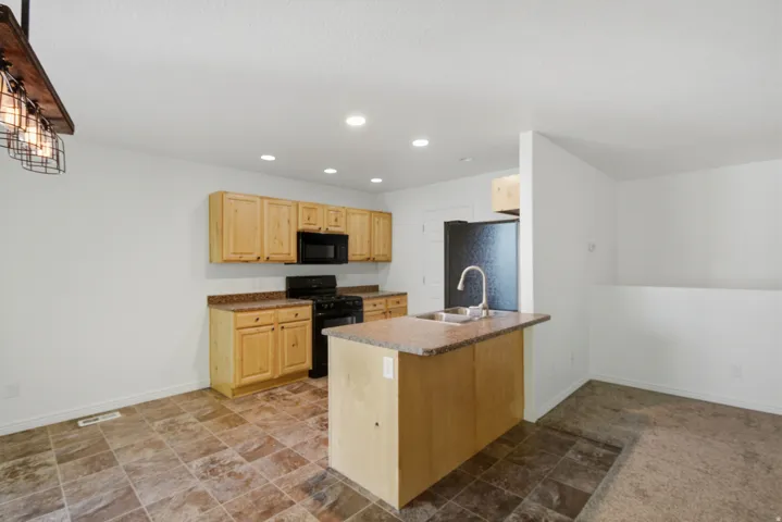 Kitchen featuring wood cabinetry, black appliances, a central island with a sink, recessed lighting, and tile flooring