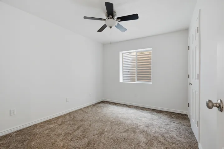 Carpeted room with white walls, a ceiling fan, and a single window