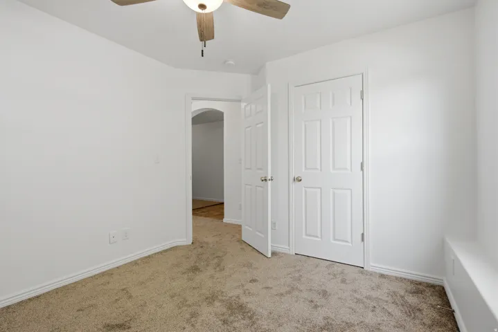 Carpeted room featuring a ceiling fan with integrated lighting, white baseboards, and two paneled interior doors