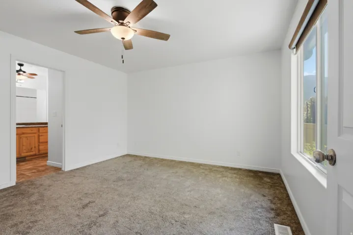 Bright interior space featuring neutral carpet, a ceiling fan with integrated lighting, and white walls