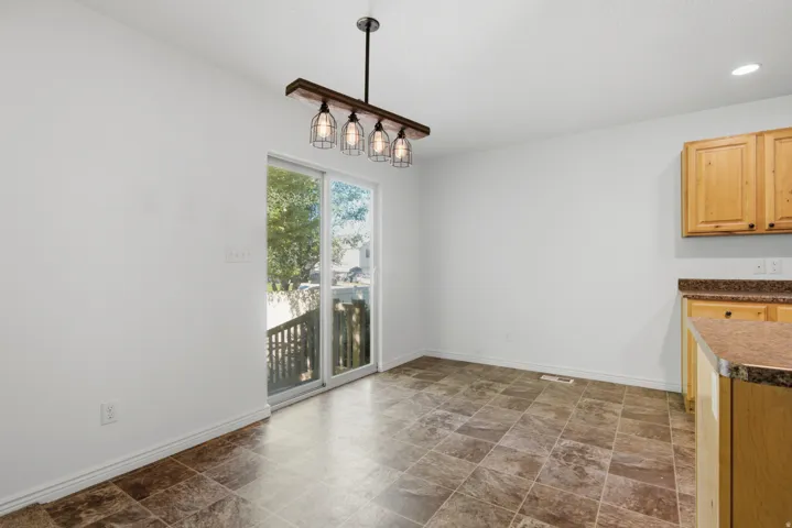 Dining area featuring a sliding glass door to exterior, a linear light fixture with wire cage shades, light wood cabinetry, and a patterned tile floor