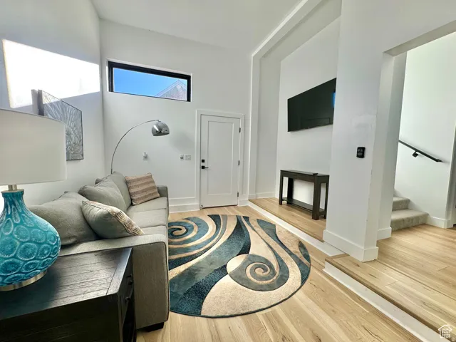 Bright living area featuring wood-finish flooring, a contemporary accent window, vaulted ceilings, a modern door, and a staircase with a dark handrail