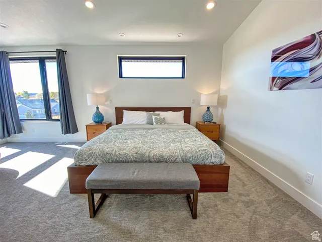 Spacious bedroom featuring light gray carpeting, recessed lighting, and a large multi-pane window with dark trim