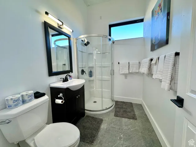 Bathroom featuring a corner shower with glass enclosure, single vanity with dark cabinetry, wall-mounted mirror, and a fixed transom window