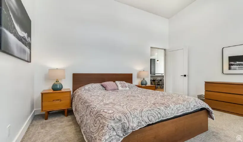 Vaulted ceiling bedroom featuring plush carpeting, crisp white walls, and a contemporary door with matte black hardware