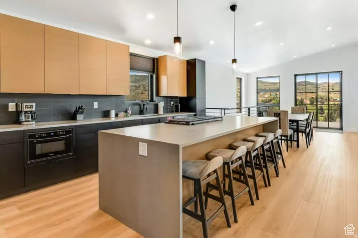 Open-concept kitchen featuring an oversized island with seating, integrated cooktop, light wood-finish flooring, and black framed windows