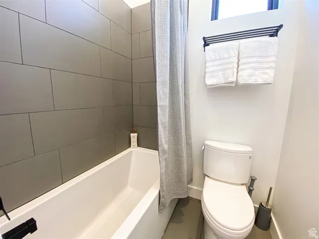 Bathroom featuring a white soaking tub with a matte black faucet, full-height gray subway tile surround, and a modern white toilet