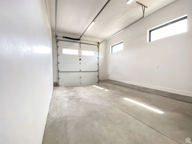 Spacious garage featuring a concrete floor, overhead lighting, and a white paneled garage door with upper window inserts