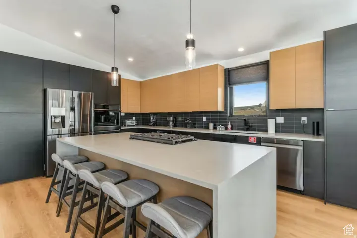 Kitchen featuring a large central island with a built-in cooktop, stainless steel appliances, dark subway tile backsplash, and two-tone cabinetry