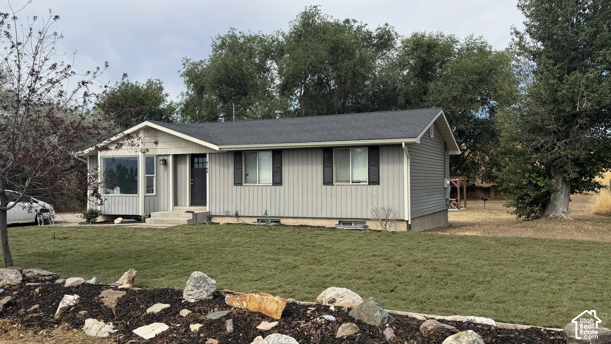 Ranch-style residence featuring light gray vertical and horizontal siding, a dark gray shingled roof, and a dark front door