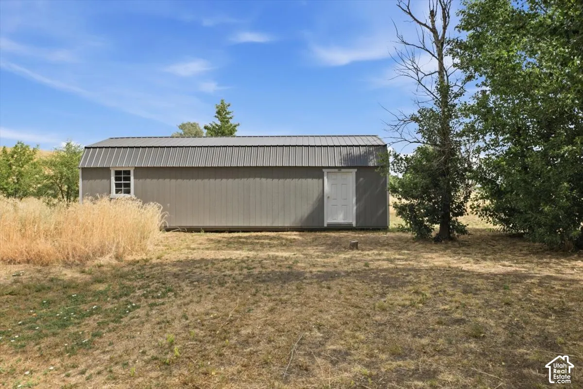 Freestanding outbuilding featuring gray metal siding, a corrugated metal gambrel roof, and a single white entry door