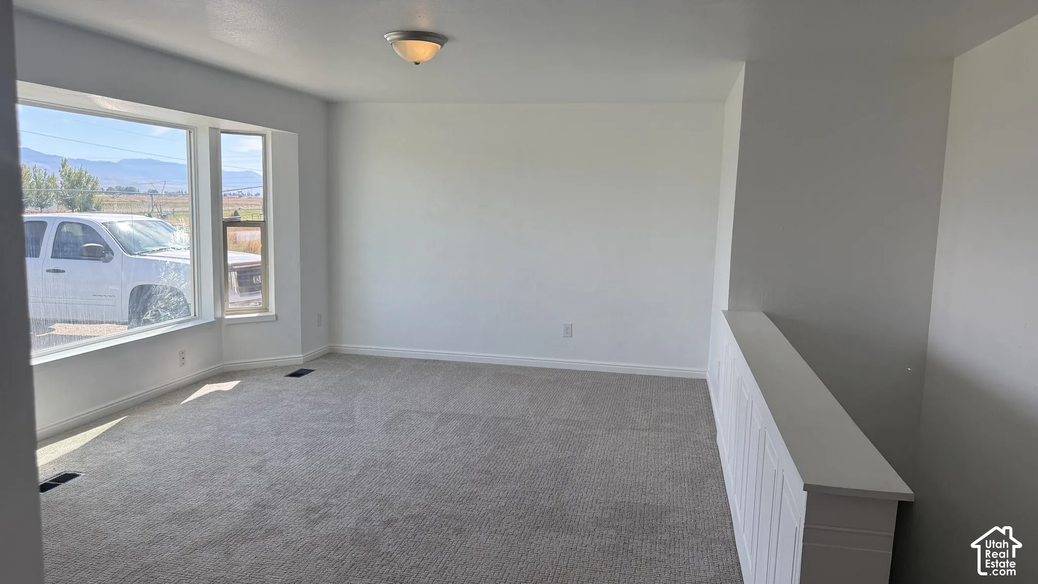 Bay window, neutral gray carpeting, overhead semi-flush mount lighting, white painted railing, and white wall finishes