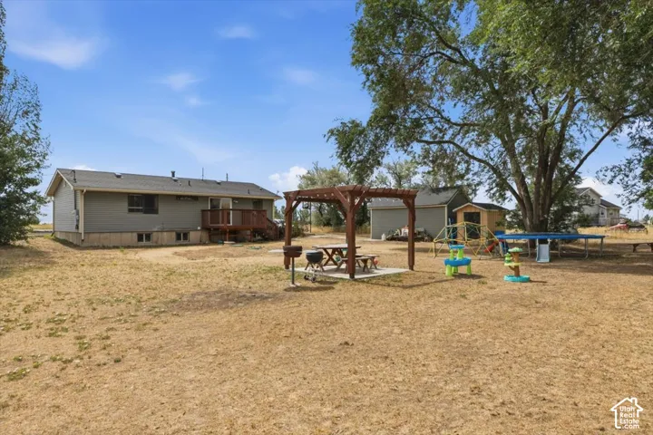 Expansive backyard featuring a shaded pergola over a concrete patio, a detached shed, a secondary building, and mature trees