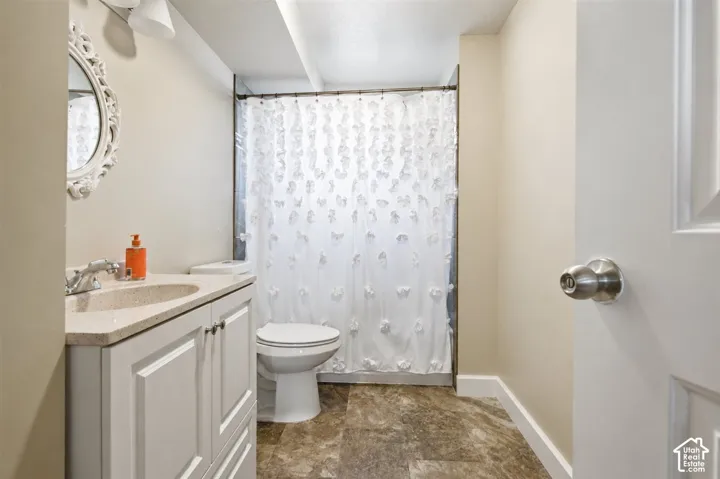 Bathroom featuring a vanity with a light-colored countertop and integrated sink, a toilet, and a shower with a white curtain