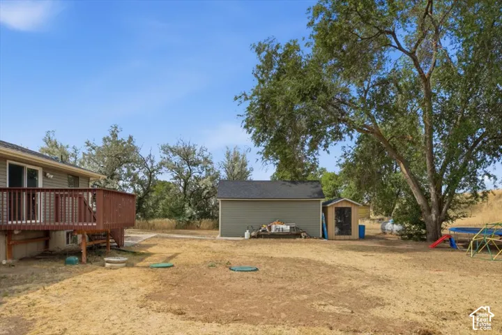 Expansive backyard featuring a wood-finish deck with railings, a detached accessory building, a secondary shed, mature trees, and open-air space