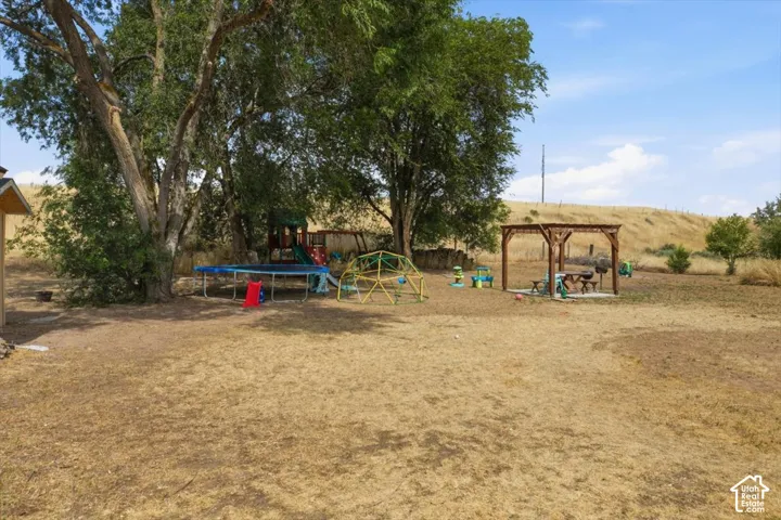 Expansive outdoor space featuring a large wooden pergola, mature trees, and a distant hillside backdrop