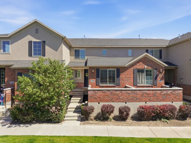 Townhome exterior featuring a brick facade with shuttered windows, a gabled entry, and a concrete pathway