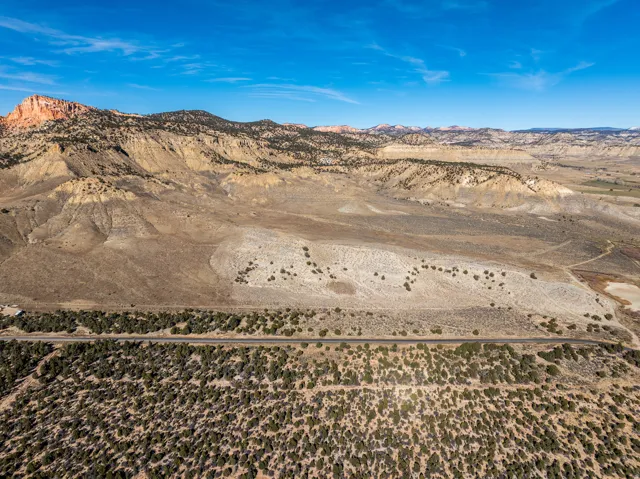 Expansive desert landscape featuring a paved road, scattered green vegetation, and distant mountains under a clear sky