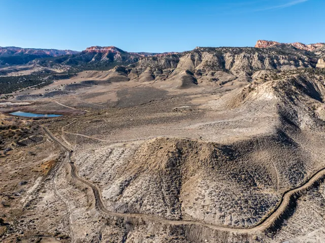 Expansive desert landscape with rolling hills, distant mesas, a natural water feature, and winding trails