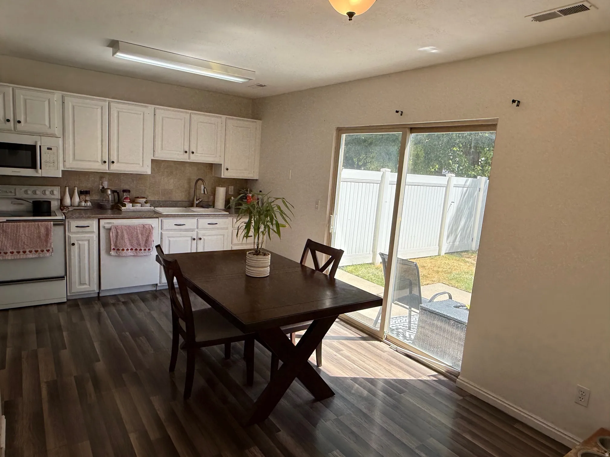 Kitchen and dining area featuring wood-finish flooring, white cabinetry, and a tile backsplash