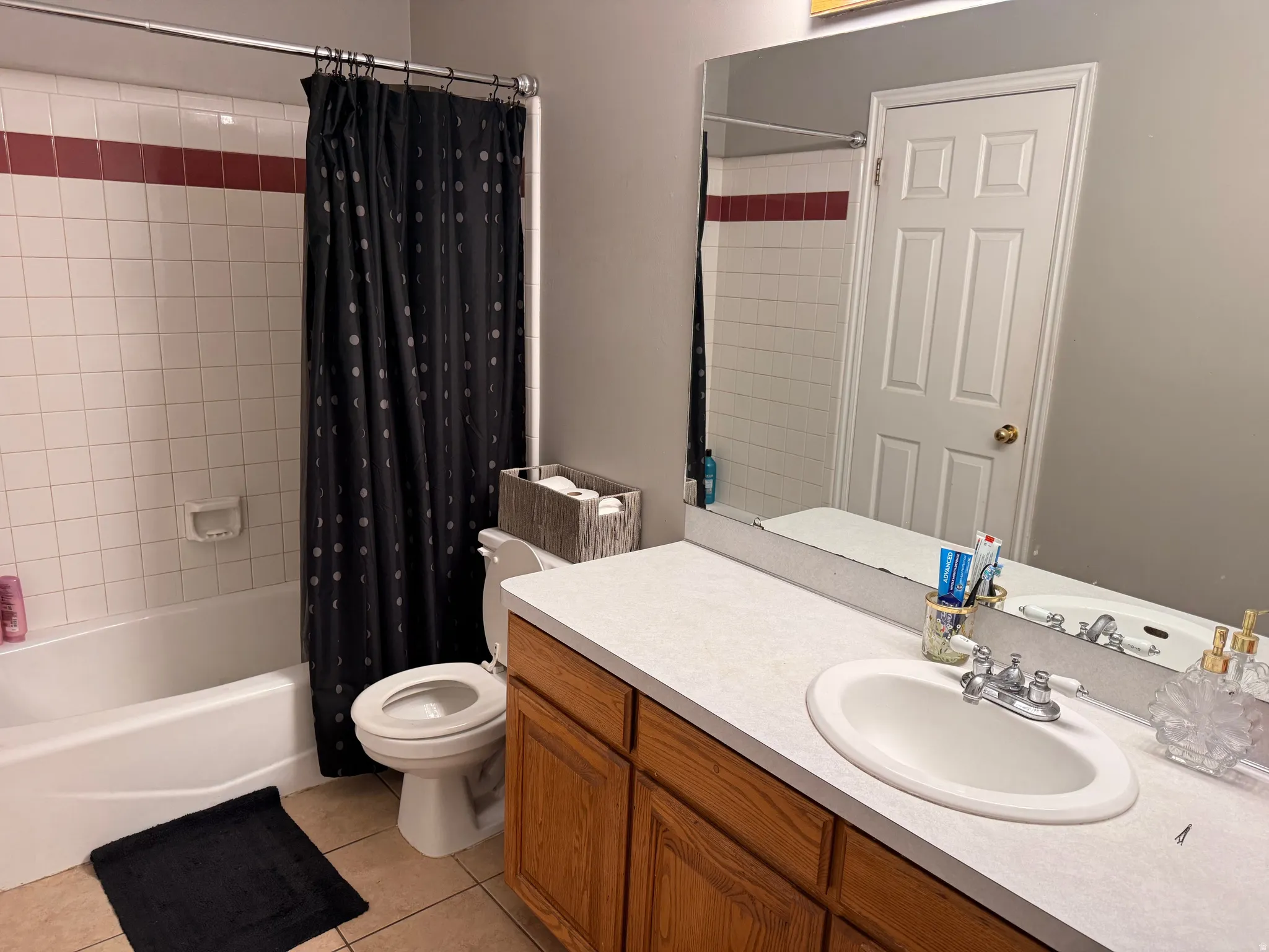 Bathroom featuring a white bathtub and shower surround with a red accent tile band, white vanity with an integrated sink, wood-finish cabinetry, and a wall-mounted mirror