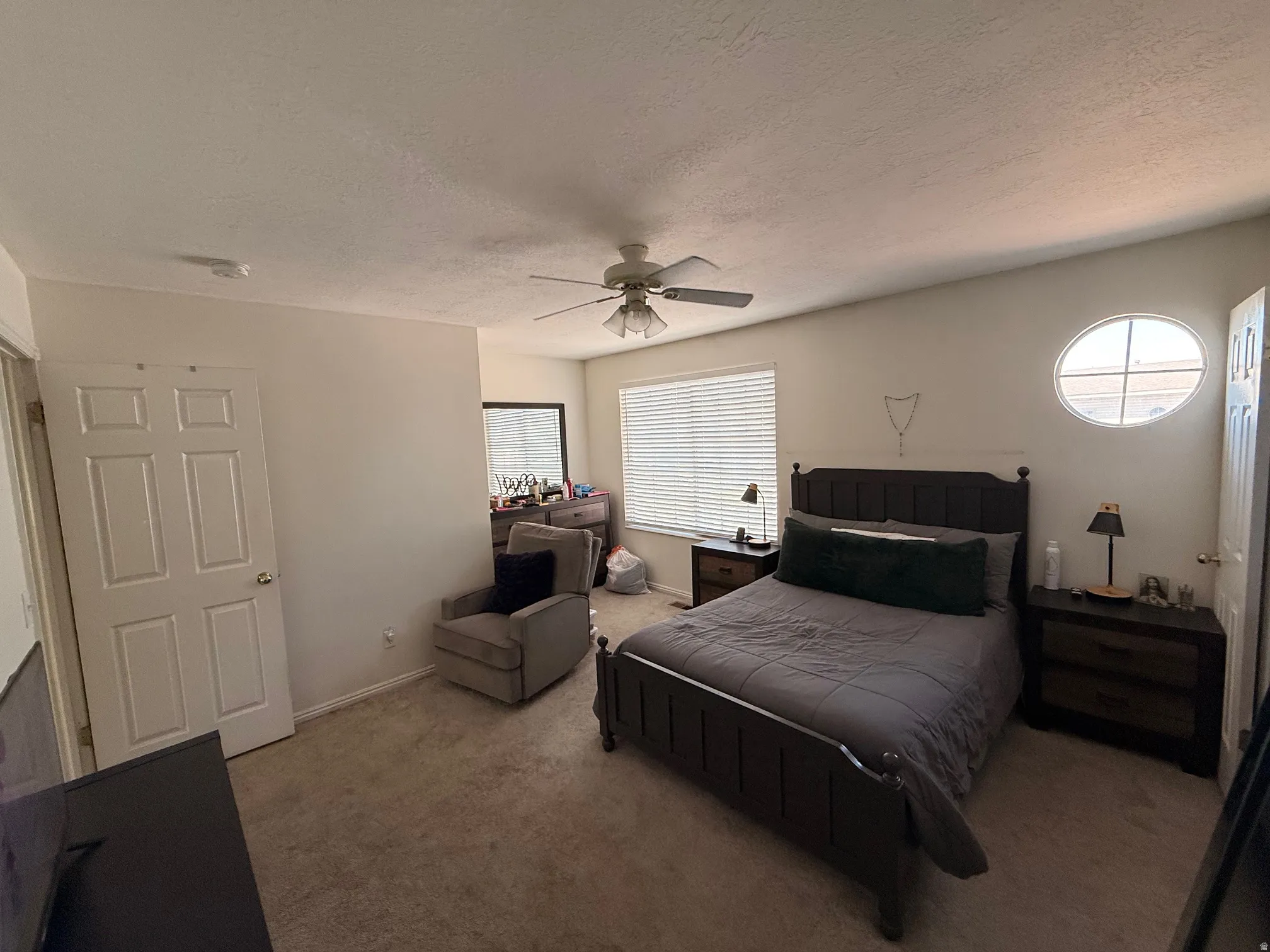 Carpeted room featuring a ceiling fan, a rectangular window with blinds, and a distinctive oval window