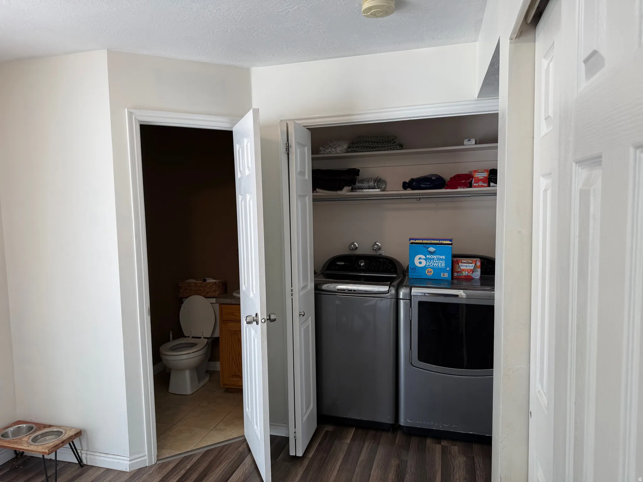 Convenient laundry closet with built-in shelving, featuring wood-finish flooring