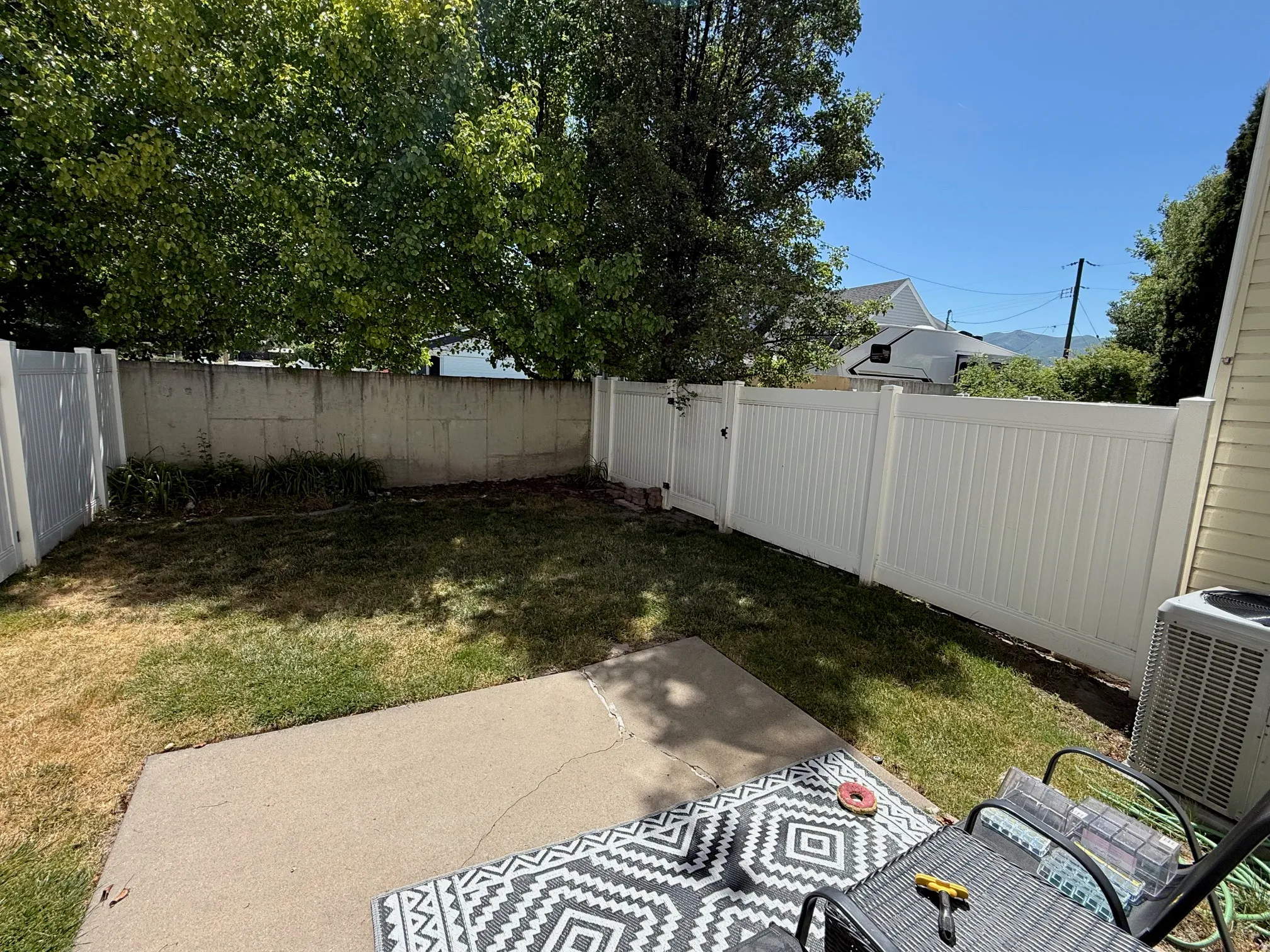Private backyard space featuring a concrete patio, a section of lawn, and a white privacy fence with a gate