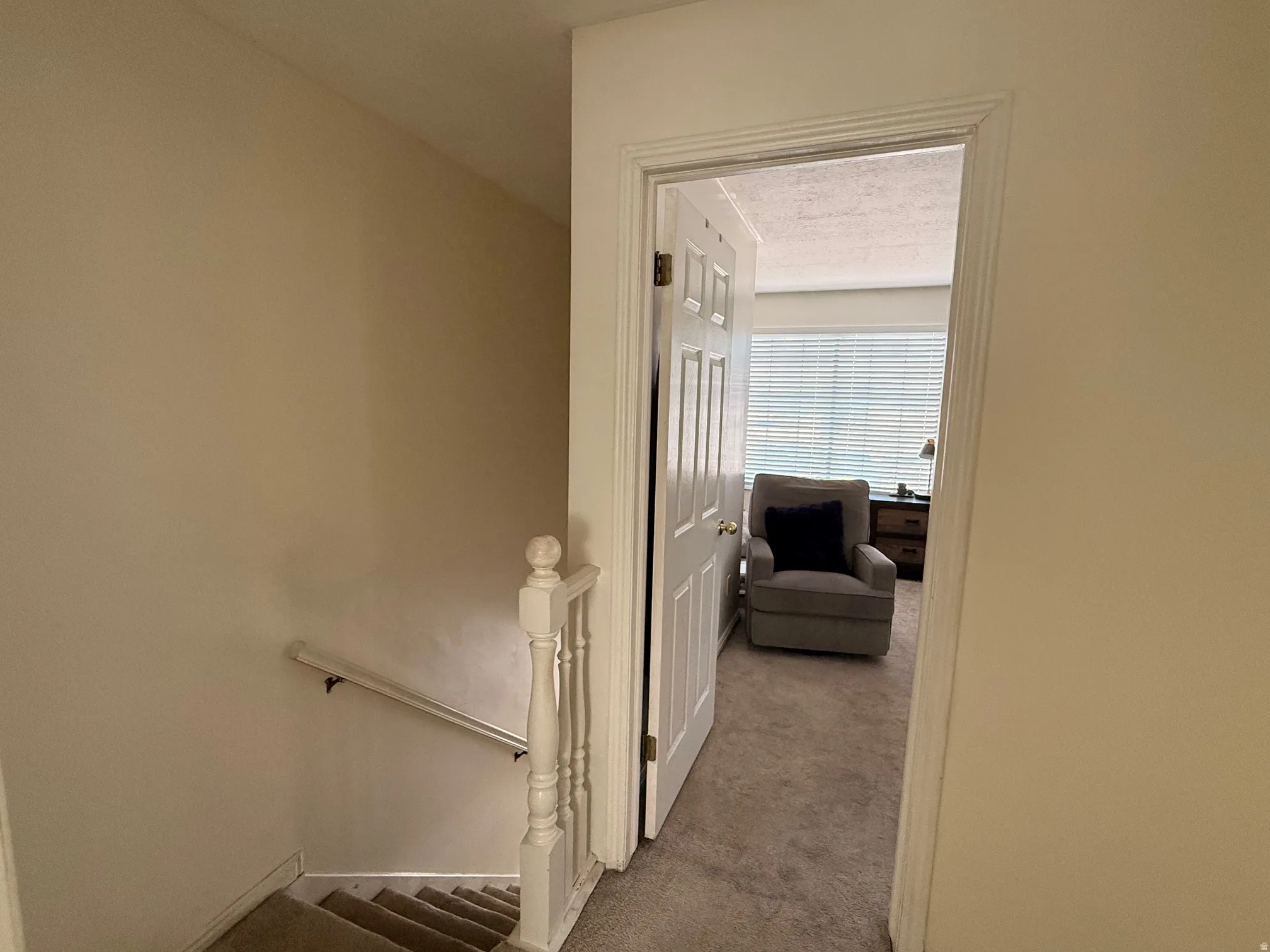 Carpeted stairs featuring a white painted handrail and balusters, leading down from a carpeted landing