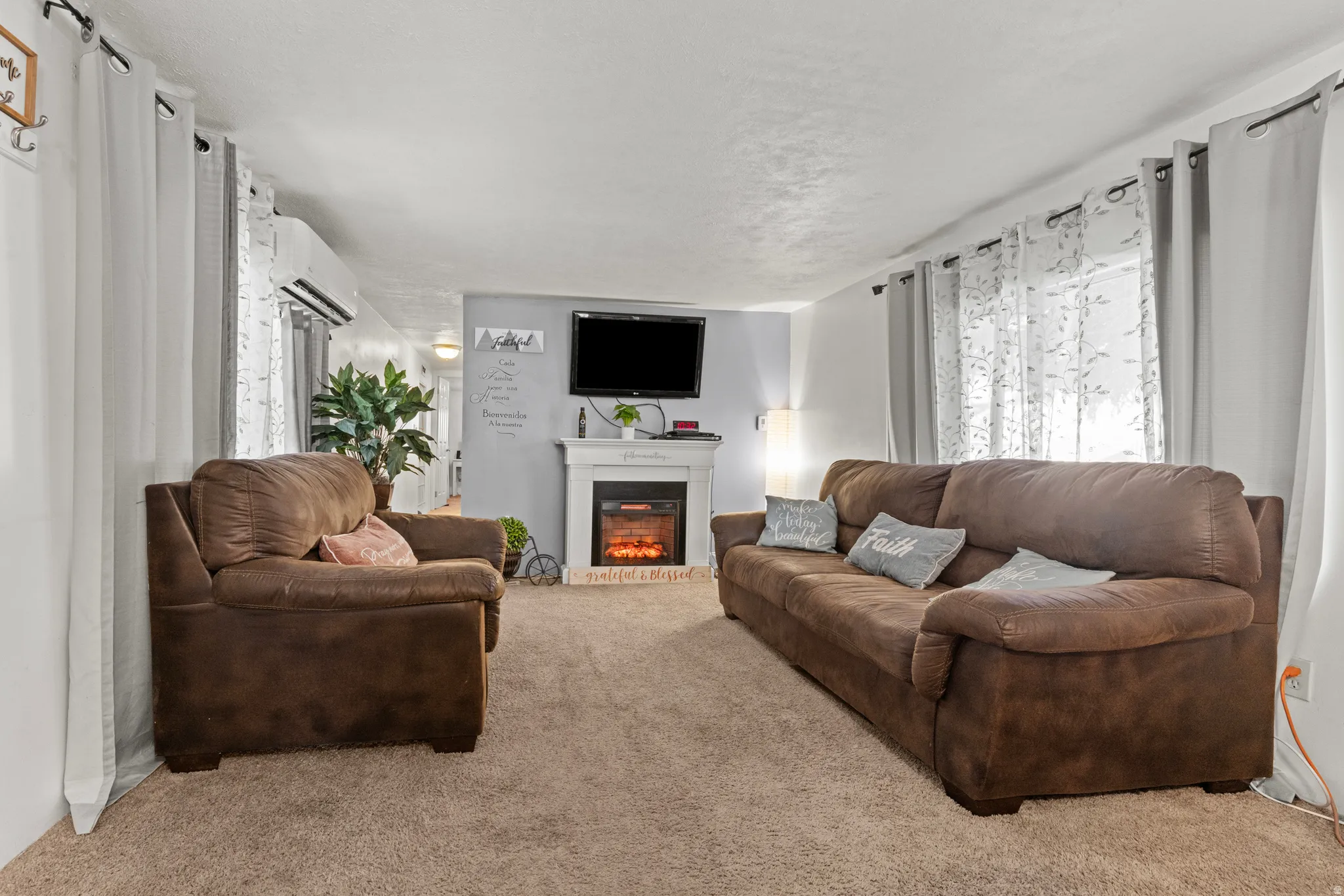 Living area featuring wall-to-wall carpeting, an integrated fireplace with a mantel, a wall-mounted television, and a window with sheer and blackout curtains