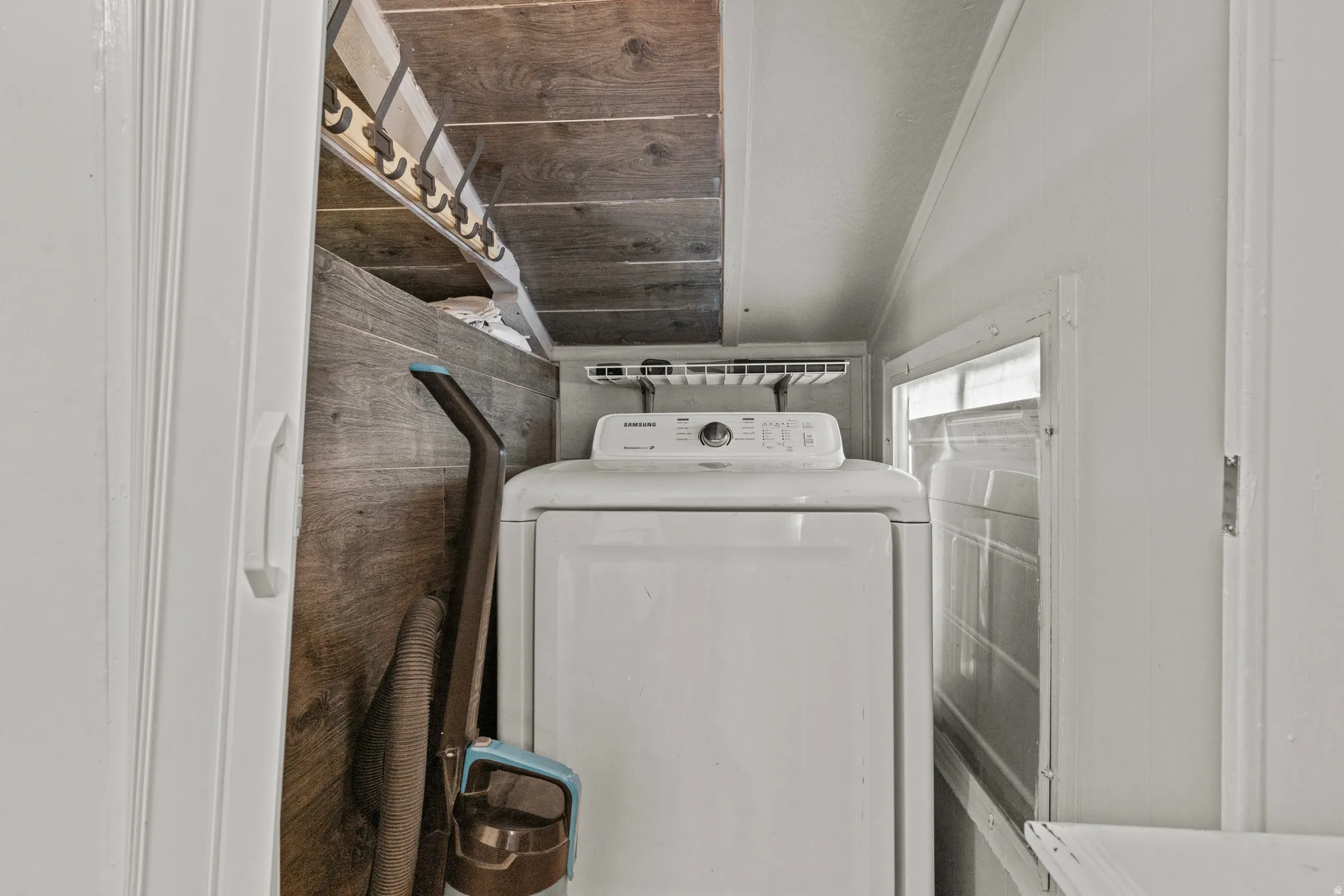 Dedicated laundry area featuring a white stackable appliance set, wood-finish wall paneling, and a built-in hanging rod